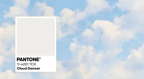 Pantone-Farbkarte "Cloud Dancer" vor einem Himmel mit Wolken. Diese zarte Farbe könnte die Farbe des Jahres 2026 sein.