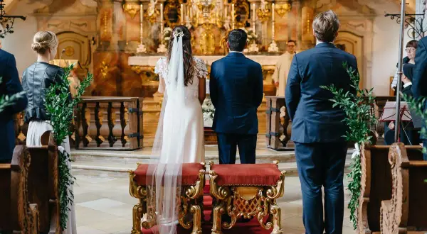 Trauzeugen stehen in der Kirche Spalier. Die Braut und der Bräutigam stehen vor dem Altar.