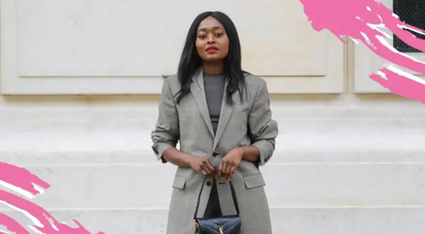 Frau in kariertem Blazer und dunklem Oberteil, perfekt für einen **business casual** Look, hält eine schwarze Handtasche.