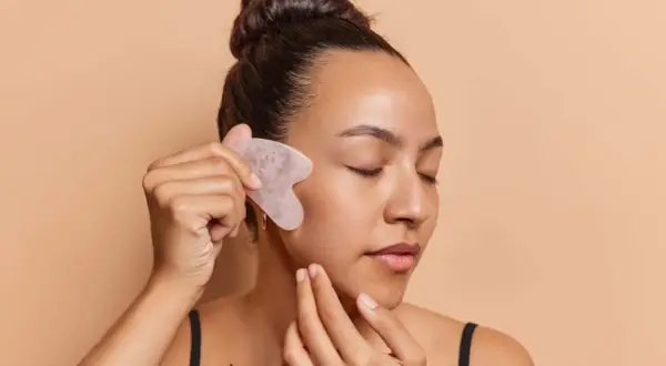 Frau mit geschlossenen Augen nutzt ein Gua Sha Stein für ihr Gesicht.
