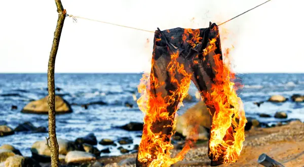 Jeans brennen am Strand, ein Symbol für den Polterabend. Die Flammen tanzen, während die Wellen rauschen.