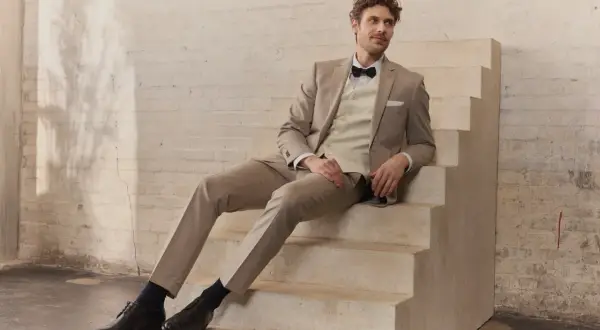 Mann in hellem Hochzeitsanzug mit Fliege sitzt auf Treppe. Perfekt für die Frage: wann Hochzeitsanzug kaufen?