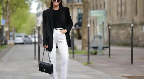 Frau in schicker Business-Kleidung mit schwarzem Blazer, weißer Hose und Chanel-Tasche.