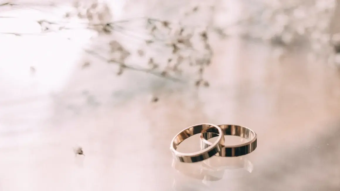 Zwei goldene Ringe liegen nebeneinander, ein Symbol für 23. hochzeitstag. Zarte Blüten im Hintergrund.