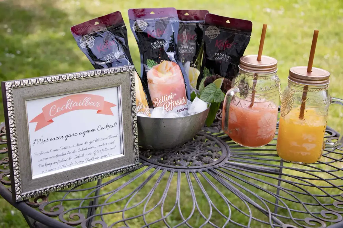 Cocktailbar-Schild und gefrorene Cocktails für eine Hochzeit. Mehrere Beutel mit gefrorenen Cocktails und zwei fertige Getränke in Gläsern mit Strohhalmen.