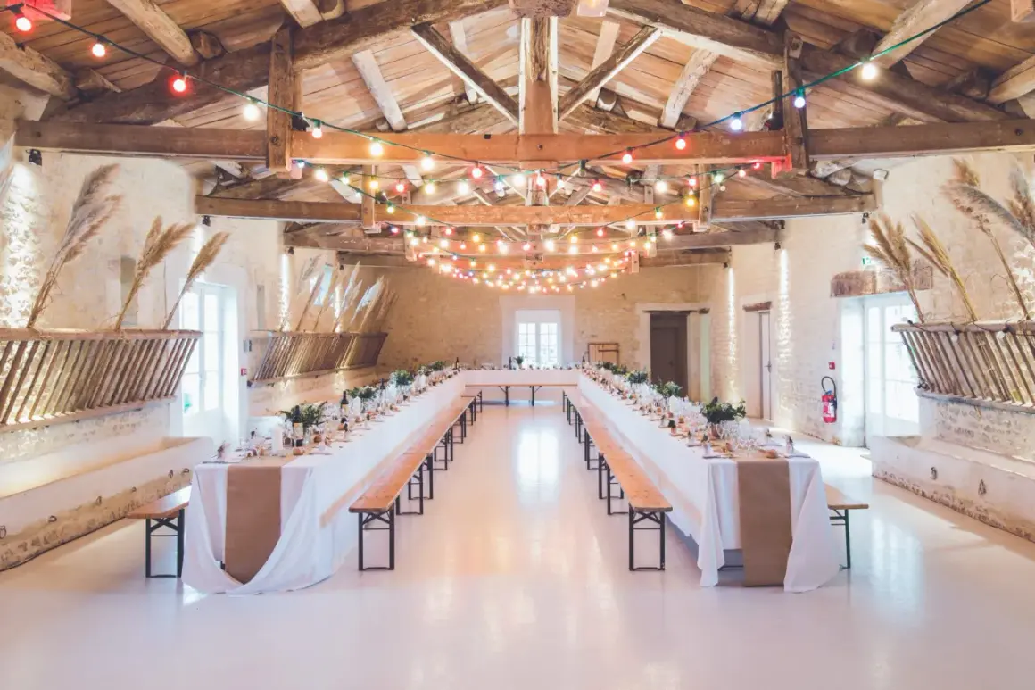 Festlich geschmückte Hochzeitsscheune mit langen Tafeln, Lichterketten und rustikalen Holzbänken.