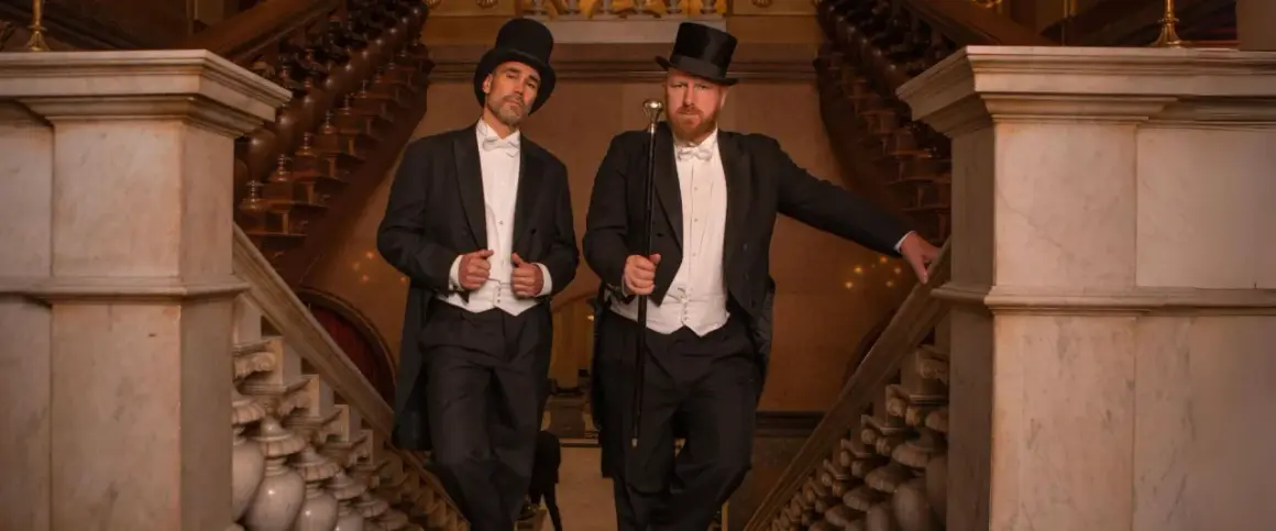 Zwei Herren im eleganten Frack mit Zylinder und Gehstock, ein perfektes Beispiel für den Dresscode Herren für einen besonderen Anlass.