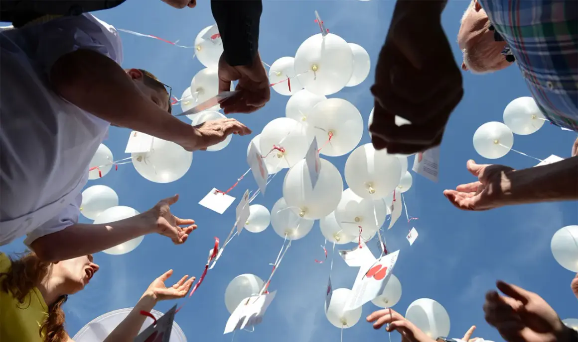 Gäste lassen bei einer Hochzeit weiße Luftballons mit Wünschen in den Himmel steigen.