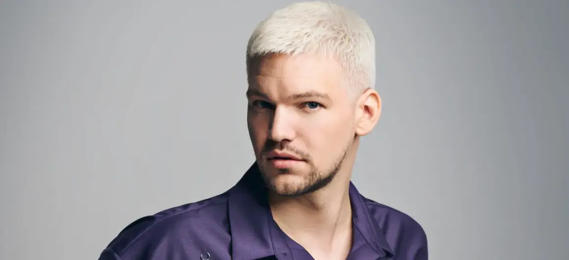 Mann mit platinblonden, kurz geschnittenen Haaren und einem Dreitagebart. Seine modernen herren frisuren unterstreichen seinen selbstbewussten Blick.
