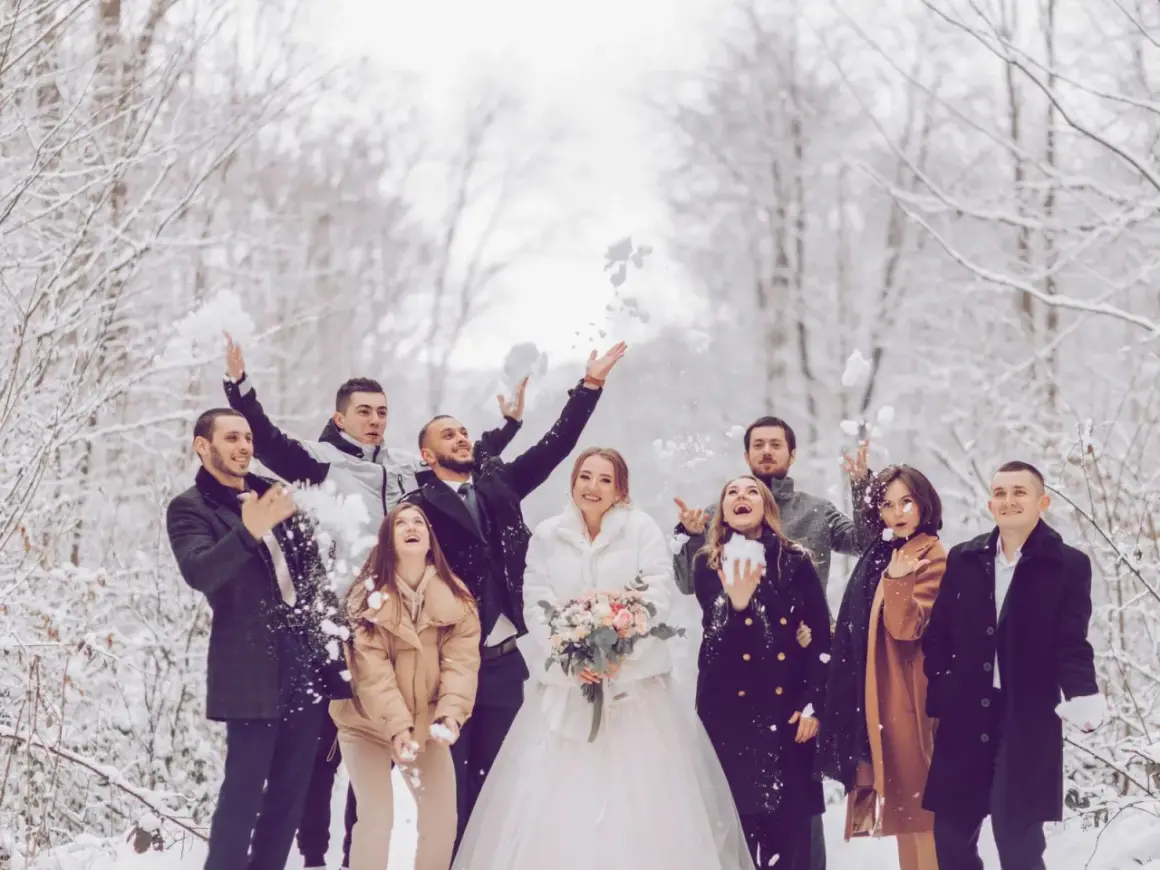 Brautpaar und Gäste werfen im Winter Schnee. Eine standesamtliche Hochzeit im Schnee mit fröhlichen Gästen.