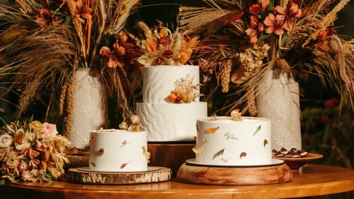 Drei weiße Hochzeitstorten, schlicht elegant dekoriert mit getrockneten Blumen und Blättern, umgeben von herbstlicher Deko.