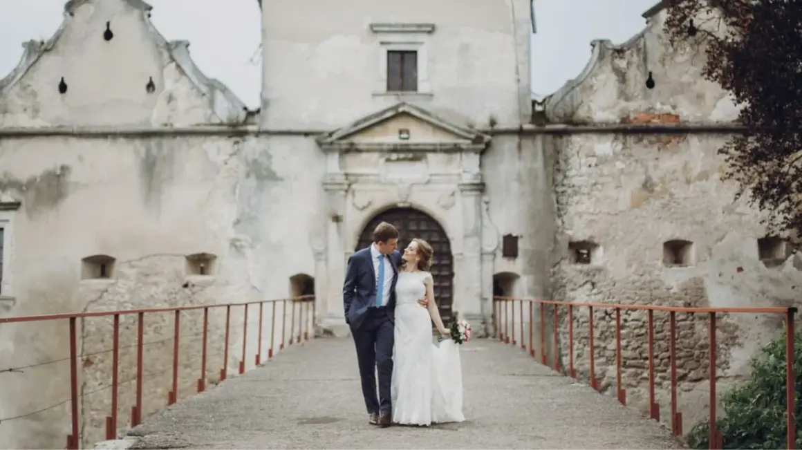 Ein Brautpaar spaziert über eine Brücke vor einer alten Burg. Die Szene erinnert an eine mittelalterliche Hochzeit.