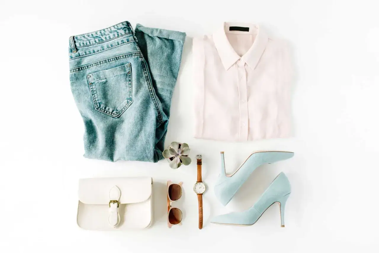 Ein minimalistischer Kleiderschrank: Jeans, hellrosa Bluse, wei&szlig;e Tasche, Sonnenbrille, Uhr, Sukkulente und hellblaue Pumps.