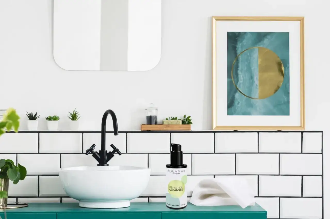 Ein moderner Waschplatz mit Waschbecken, Armatur und einem Produkt für die gesichtspflege routine. Kleine Pflanzen und ein Kunstwerk schmücken die Szene.
