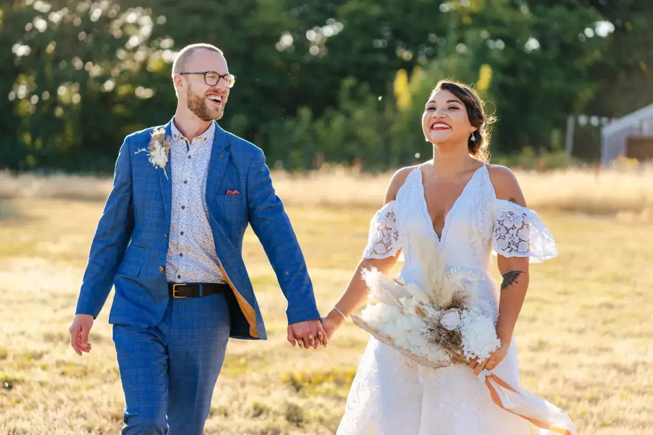 Glückliches Brautpaar im Freien. Er trägt ein blau kariertes Jackett, ein gemustertes Hemd und eine Hose – ein stilvolles Hochzeitsoutfit Mann ohne Anzug.