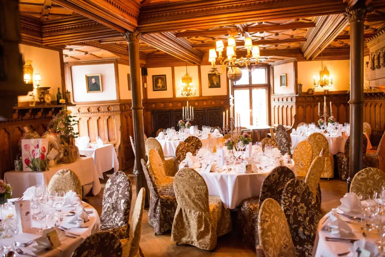 Festlich gedeckte Tische in einem holzget&auml;felten Raum, bereit f&uuml;r eine mittelalterliche Hochzeit.