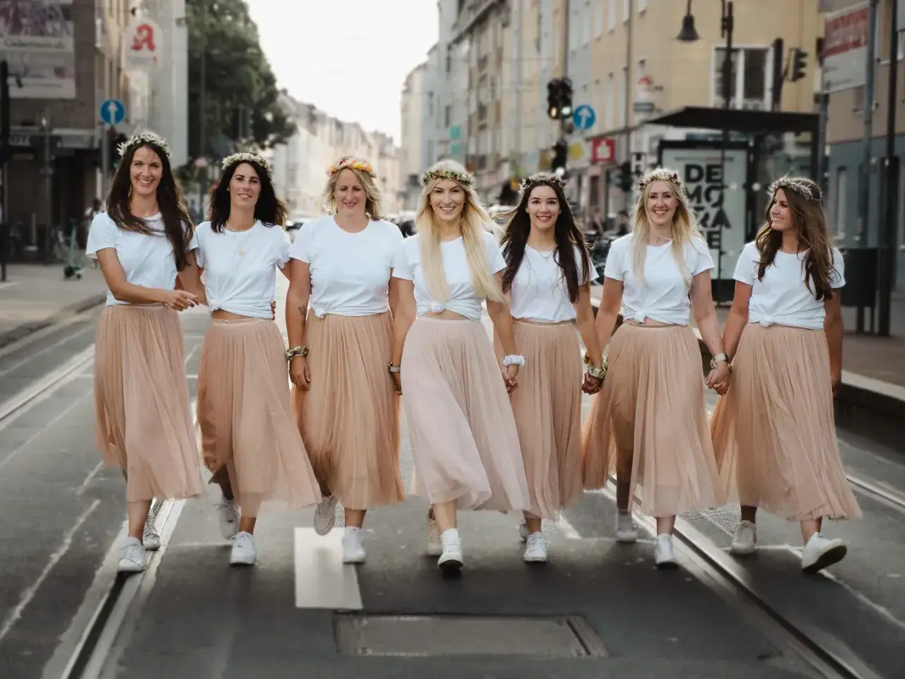 Sieben Frauen mit Blumenkr&auml;nzen und passenden R&ouml;cken &uuml;berqueren fr&ouml;hlich eine Stra&szlig;e. Ein toller Geheimtipp f&uuml;r einen Junggesellenabschied!