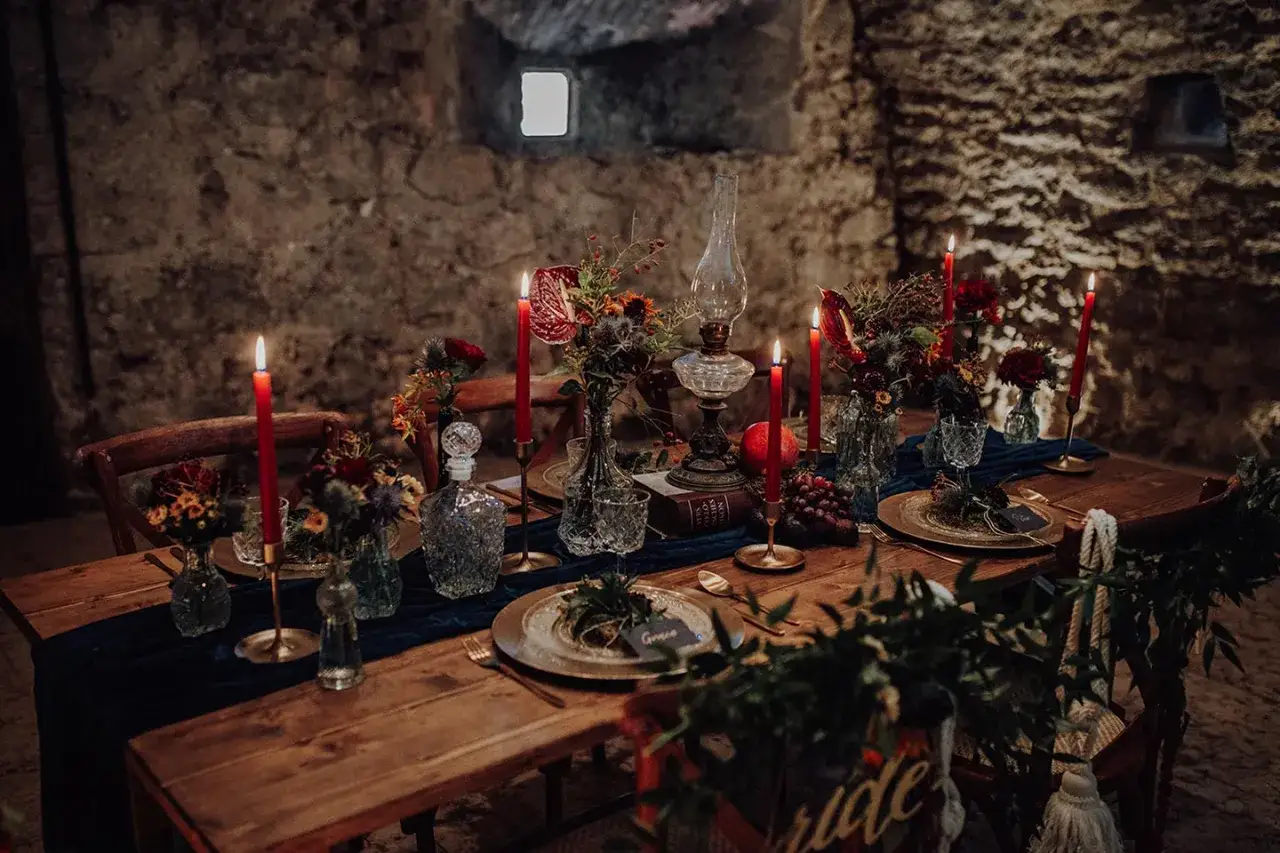 Romantische mittelalter hochzeit Tafel mit Kerzen, Blumen und Trauben. Dunkle, stimmungsvolle Beleuchtung in einer Burg.