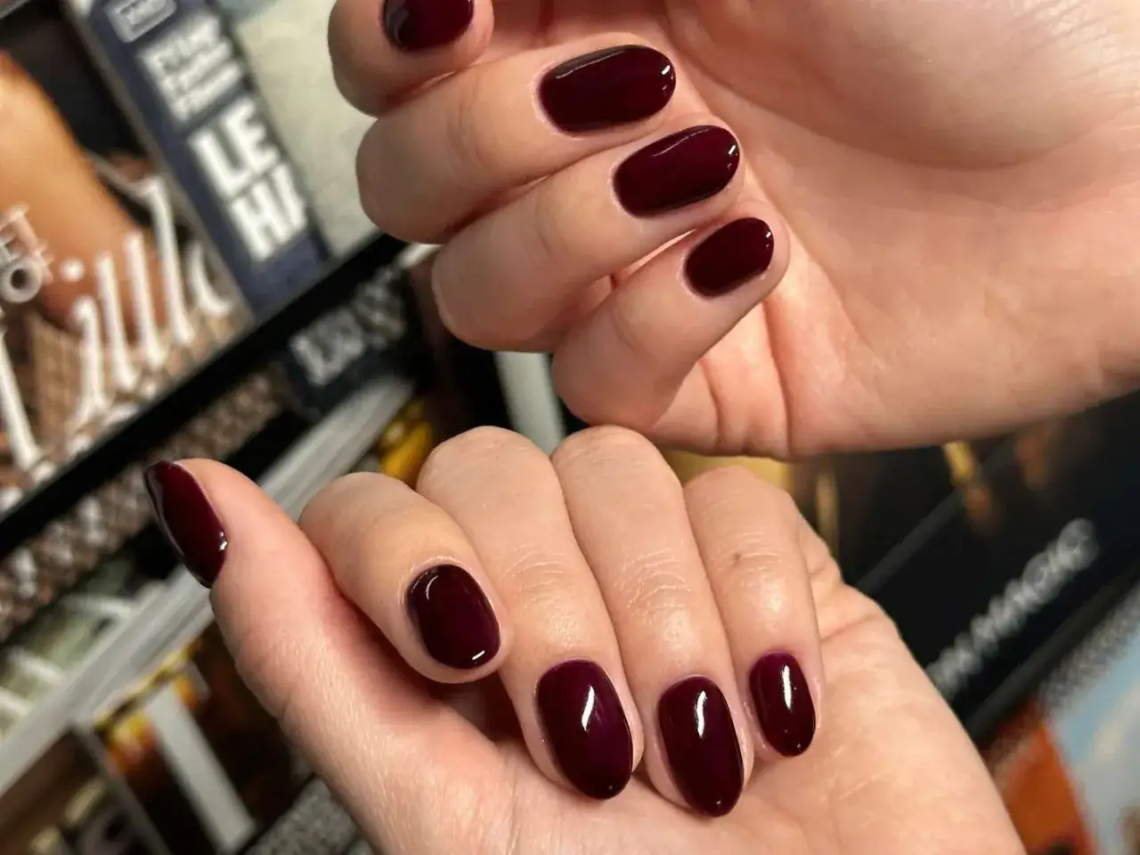 Elegante, dunkelrote Nägel, ein Trend für 2026, glänzen vor einem unscharfen Hintergrund aus Magazinen.
