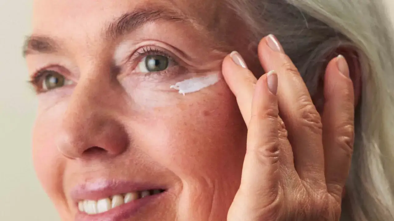 Eine Frau um die 60 trägt eine Creme auf, um kleine Pickel im Augenbereich zu behandeln.