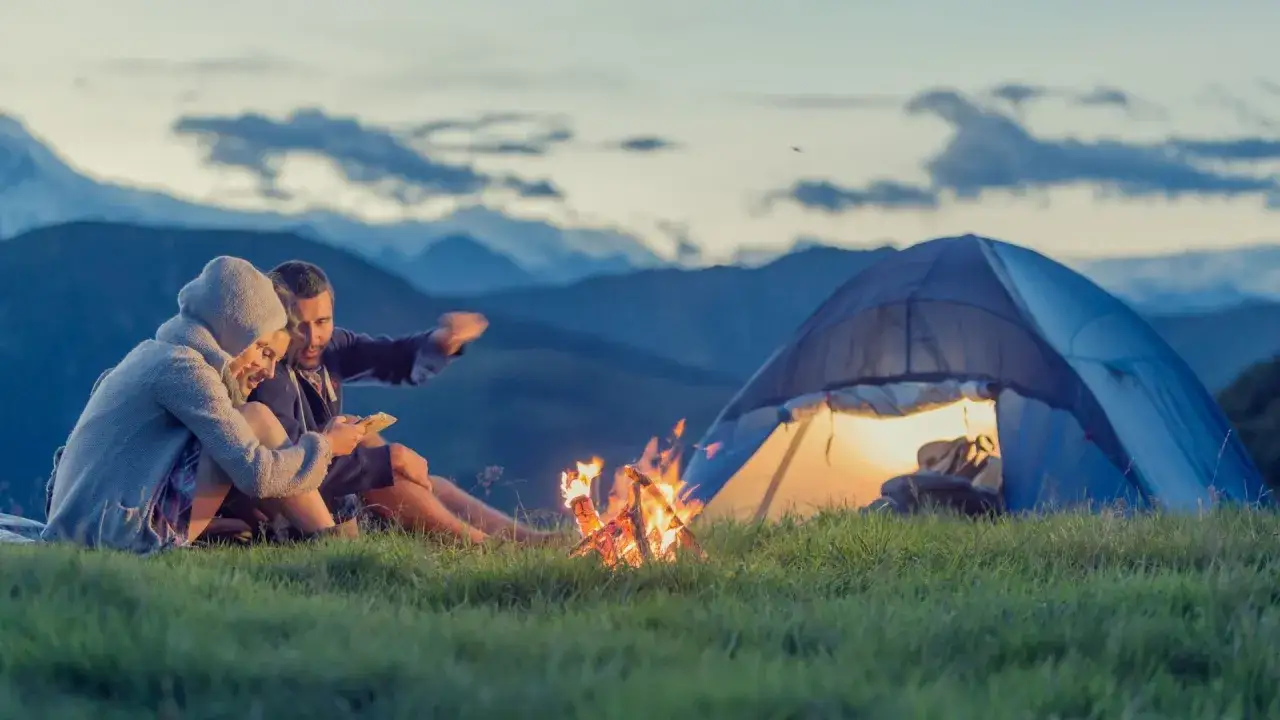 Ein Paar sitzt am Lagerfeuer vor einem Zelt in den Bergen. Ein Traum auf ihrer Bucket List wird wahr.