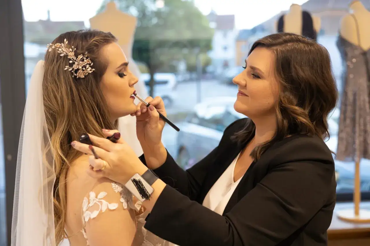 Braut wird geschminkt, bereit für die Hochzeit. Make-up-Artistin trägt Lippenstift auf.