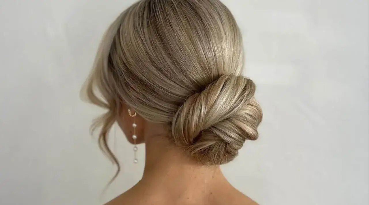 Eleganter, tiefer Dutt für die Hochzeit, mit sanften Wellen und Perlenohrringen.