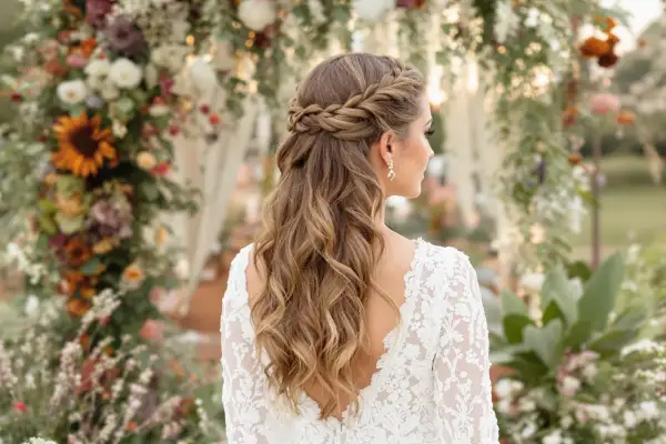 Eine Braut mit einer wunderschönen, geflochtenen Boho-Frisur steht vor einem üppigen Blumenbogen.