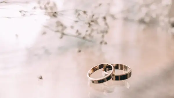 Zwei goldene Ringe liegen nebeneinander, ein Symbol für 23. hochzeitstag. Zarte Blüten im Hintergrund.