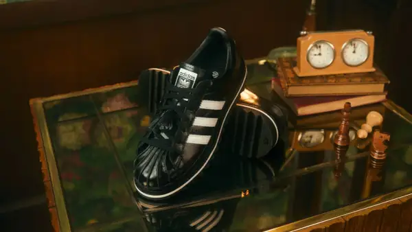 Schwarze Adidas Superstar Sneaker mit weißen Streifen, ein stilvolles Statement für aktuelle Sneaker Trends Herren. Schachfiguren und eine Spieluhr deuten auf eine strategische Eleganz hin.