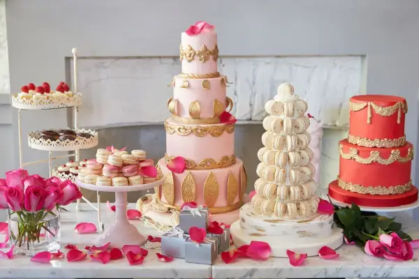 Ein prachtvolles Kuchenbuffet für eine Hochzeit: mehrstöckige Torten in Rosa und Rot, Macarons-Türme und Rosen.