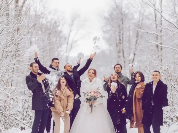 Brautpaar und Gäste werfen im Winter Schnee. Eine standesamtliche Hochzeit im Schnee mit fröhlichen Gästen.