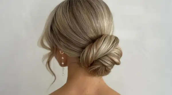 Elegante Hochzeitsfrisur mit einem kunstvoll gedrehten Dutt und zarten Perlenohrringen. Perfekt für den großen Tag.