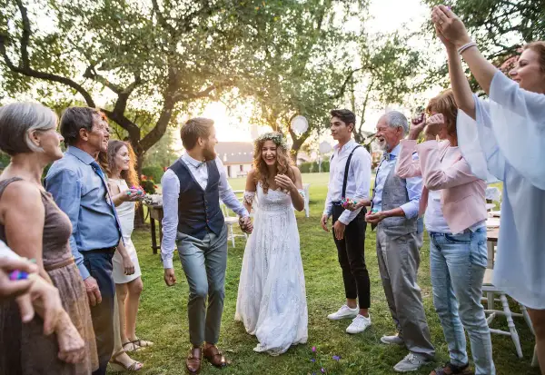 Brautpaar feiert mit Familie und Freunden. Konfetti fliegt, die Stimmung ist ausgelassen. Eine fröhliche Hochzeit, bei der die Farben der Kleidung und des Konfettis im Sonnenlicht leuchten.