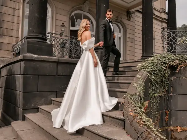 Brautpaar auf Treppe, sie trägt ein elegantes weißes schleppe brautkleid, er im schwarzen Anzug.