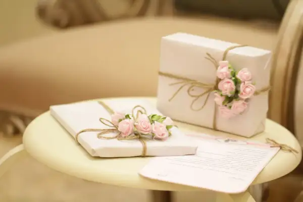 Zwei Geschenke, mit rosa Rosen und Juteband verziert, stehen auf einem Tisch. Ein Brief liegt daneben. Ein schönes Bild, das die Bedeutung des 14. Hochzeitstags unterstreicht.
