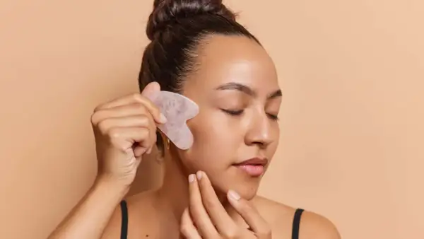 Frau mit geschlossenen Augen nutzt ein Gua Sha Stein für ihr Gesicht.