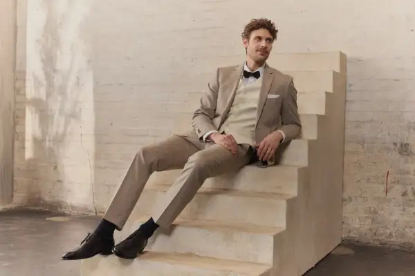 Mann in hellem Hochzeitsanzug mit Fliege sitzt auf Treppe. Perfekt für die Frage: wann Hochzeitsanzug kaufen?