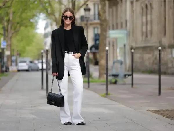Frau in schicker Business-Kleidung mit schwarzem Blazer, weißer Hose und Chanel-Tasche.